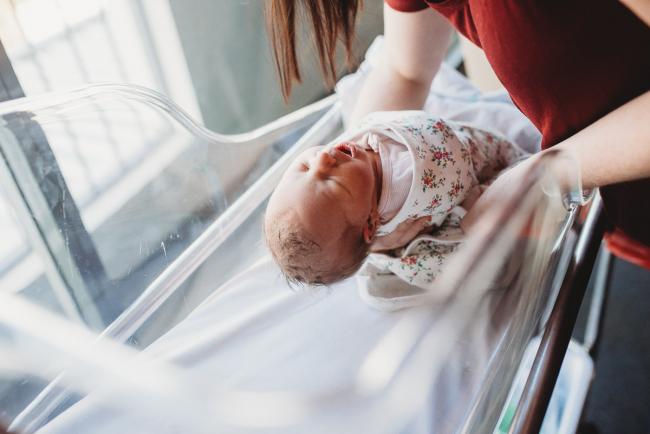 Mother placing new baby in bassinet during a Perth Fresh 48 photography session at SJOG Mt Lawley