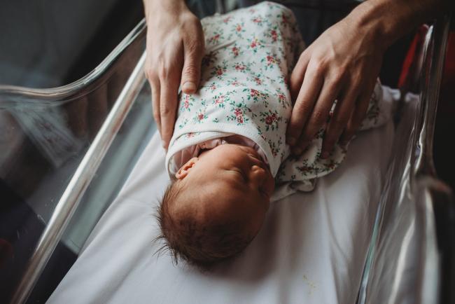 Father's hands on wrapped baby in bassinet during a Perth Fresh 48 photography session at SJOG Mt Lawley