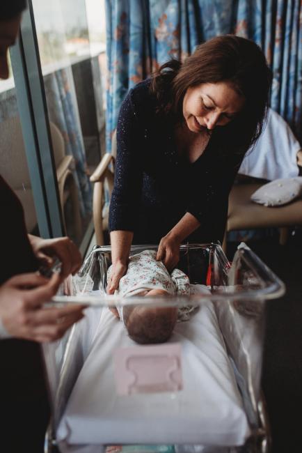 Grandmother leaning into bassinet of new baby during a Perth Fresh 48 photography session at SJOG Mt Lawley