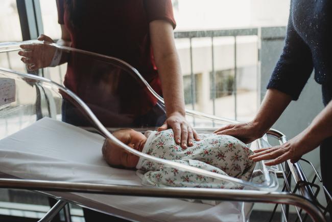 Mother and father's hands on baby in a bassinet during a Perth Fresh 48 photography session at SJOG Mt Lawley