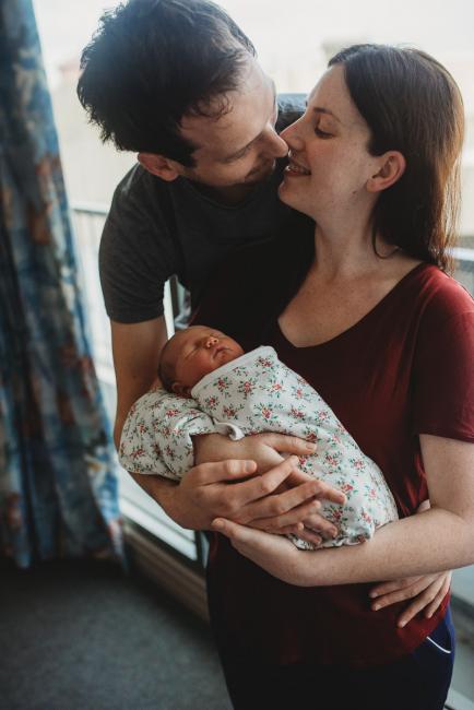 Mother and father leaning in to kiss as they hold their new baby daughter during a Perth Fresh 48 photography session at SJOG Mt Lawley