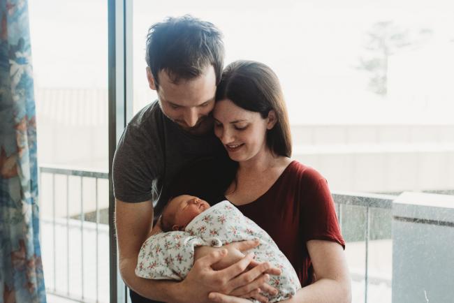 Mother and father embracing as they hold their new baby daughter during a Perth Fresh 48 photography session at SJOG Mt Lawley