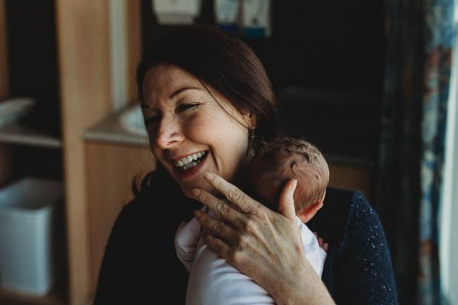 Grandmother holding baby against her shoulder and laughing during a Perth Fresh 48 photography session at SJOG Mt Lawley