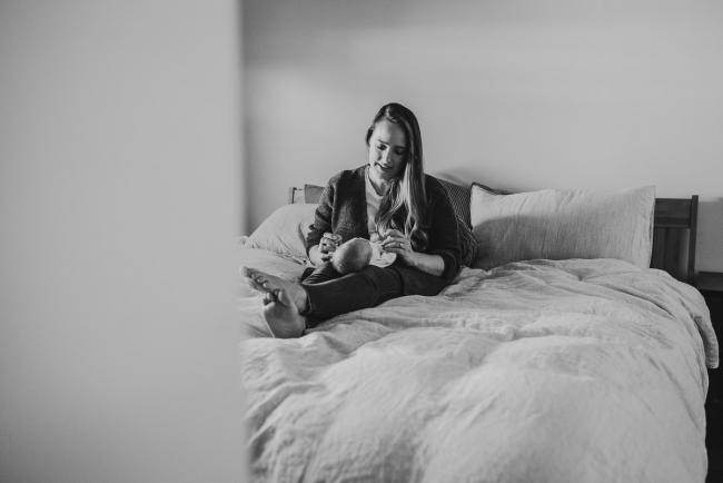 black and white image of mother laying on her bed with baby across her legs with lifestyle newborn photographer Perth