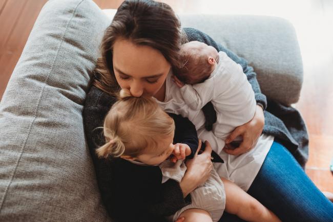 mother sitting on the couch with toddler and new baby on her lap with lifestyle newborn photographer Perth
