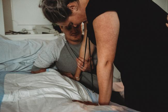 Pregnant woman leaning over the bed as her husband holds her arm with Perth birth photographer at the Family Birthing Centre