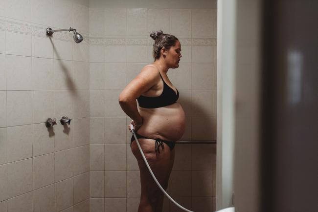 Pregnant woman standing in the shower during labour with Perth Birth Photographer at The Family Birthing Centre