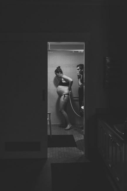 Black and white image of pregnant woman in the shower with her husband behind her with Perth Birth Photographer at The Family Birthing Centre