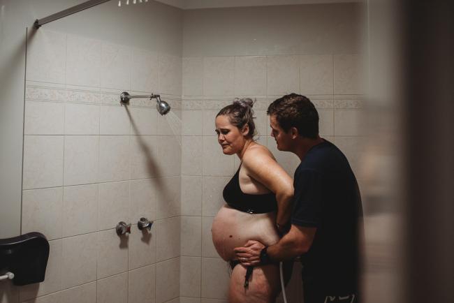 Pregnant woman standing in the shower during labour with Perth Birth Photographer at The Family Birthing Centre