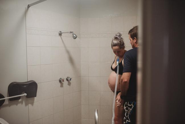 Looking through the doorway at pregnant woman and husband in the shower during labour with Perth Birth Photographer at The Family Birthing Centre