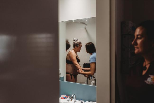 Looking into the mirror at a pregnant woman and midwife talking as another midwife looks on with Perth birth photographer at the Family Birthing Centre