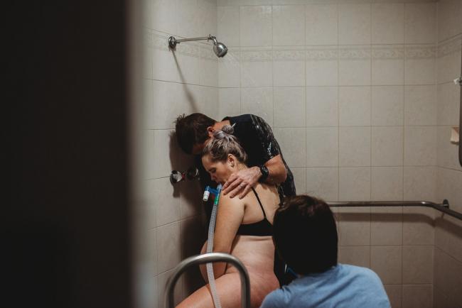 Pregnant woman squatting on the floor in the bathroom about to deliver her baby with Perth Birth Photographer at The Family Birthing Centre