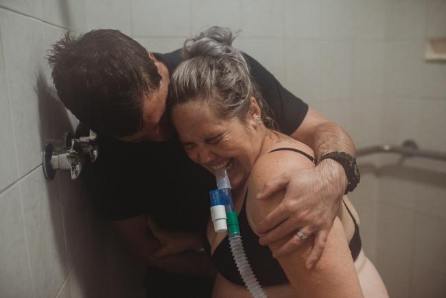 Pregnant woman pushing her baby out in the shower with Perth birth photographer at the Family Birthing Centre