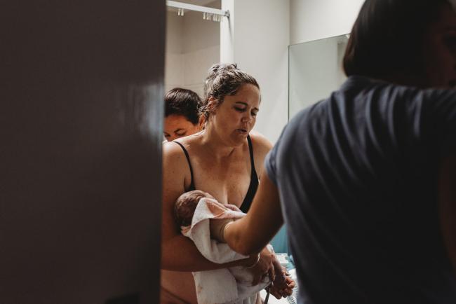 Mother carrying her newborn baby out of the bathroom with Perth Birth Photographer at The Family Birthing Centre