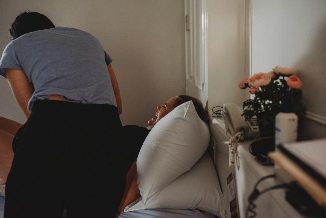 Pregnant woman on a bed being examined by the midwife with Perth birth photographer at the Family Birthing Centre