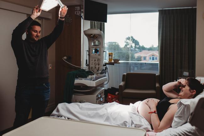 Birth-Photographer-Perth-10-of-60 Father shining hospital light on his pregnant wife in the hospital bed with Perth Birth Photographer at SJOG Mt Lawley