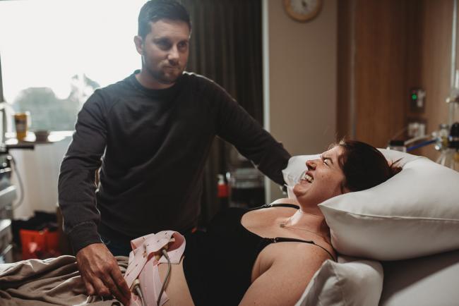 Pregnant woman during a contraction on hospital bed with partner by her side with Birth Photographer Perth at SJOG Mt Lawley