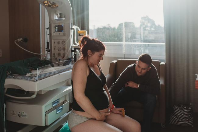 Pregnant woman on fit ball with partner leaning over to her with Birth Photographer Perth at SJOG Mt Lawley