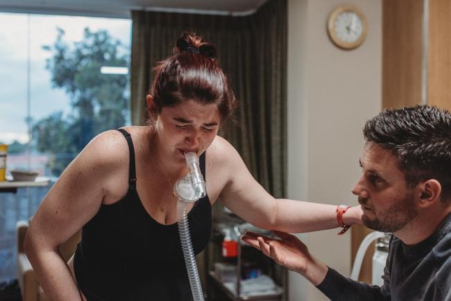 Birth-Photographer-Perth-35-of-60 Labouring mother using gas during contraction and holding onto partner with Perth Birth Photographer at SJOG Mt Lawley