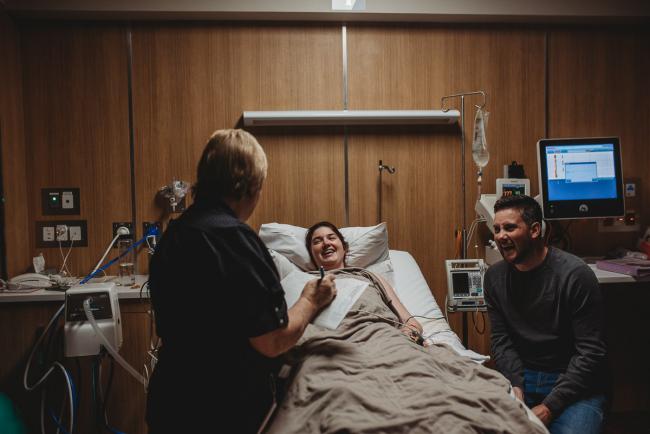 Birth-Photographer-Perth-46-of-60 Pregnant woman laughing in hospital bed with partner and midwife with Perth Birth Photographer at SJOG Mt Lawley