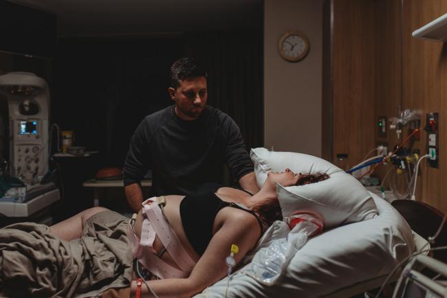 Birth-Photographer-Perth-51-of-60 Pregnant woman leaning back in pain on hospital bed as partner is by her side with Perth Birth Photographer at SJOG Mt Lawley