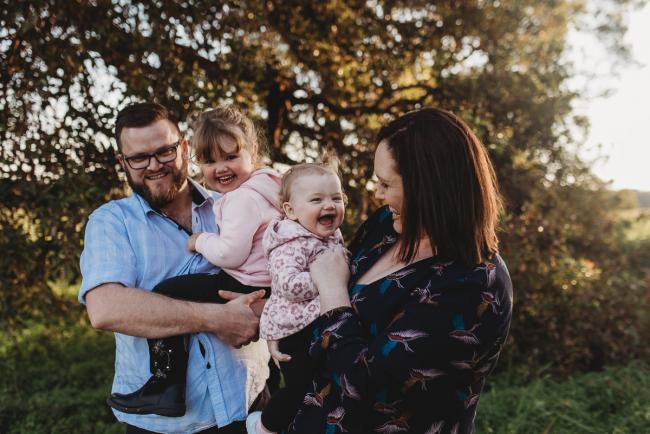Mother and father holding daughters and laughing during Perth family photography session at Perry's Paddock during golden hour