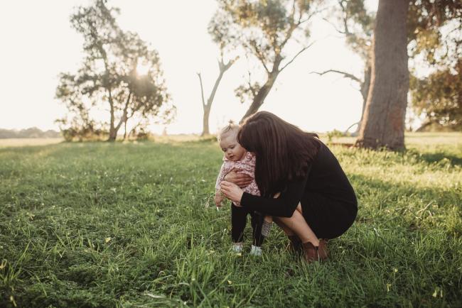 Woman squatting down next to little girl on grass during Perth family photography session at Perry's Paddock during golden hour
