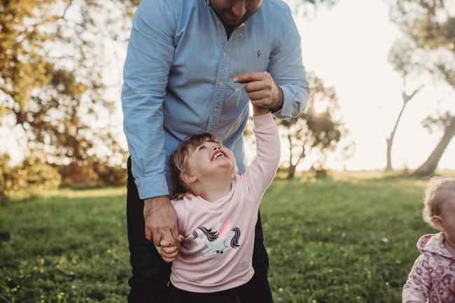 Little girl reaching up to smile at man during Perth family photography session at Perry's Paddock during golden hour