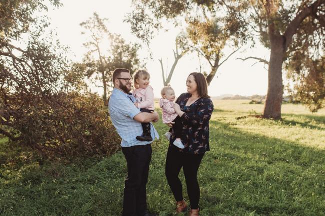 Mother and father holding daughters and laughing during Perth family photography session at Perry's Paddock during golden hour