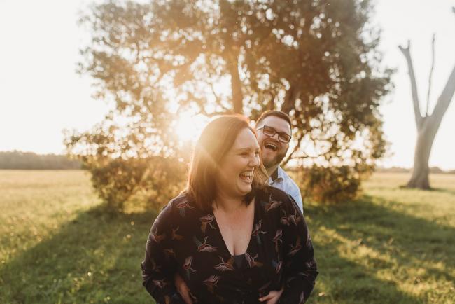 Woman laughing as husband hugs her from behind during Perth couples photography session at Perry's Paddock during golden hour