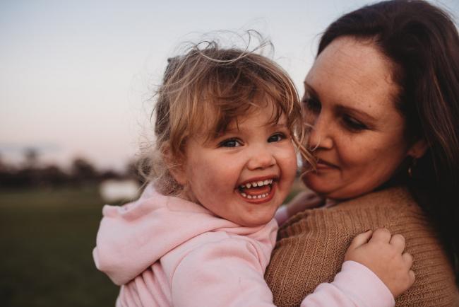 Little girl laughing as mother holds her during Perth family photography session at Perry's Paddock during golden hour
