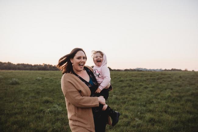 Mother holding daughter as they laugh and run during Perth family photography session at Perry's Paddock during golden hour