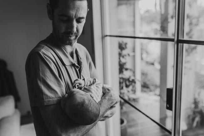 black and white image of father holding new baby by the window with Lifestyle Newborn Photographer Perth