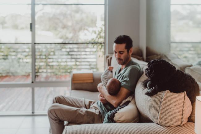 Father holding baby on the couch with dog with Lifestyle Newborn Photographer Perth