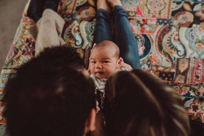 Parents holding new baby out on their legs with Lifestyle Newborn Photographer Perth