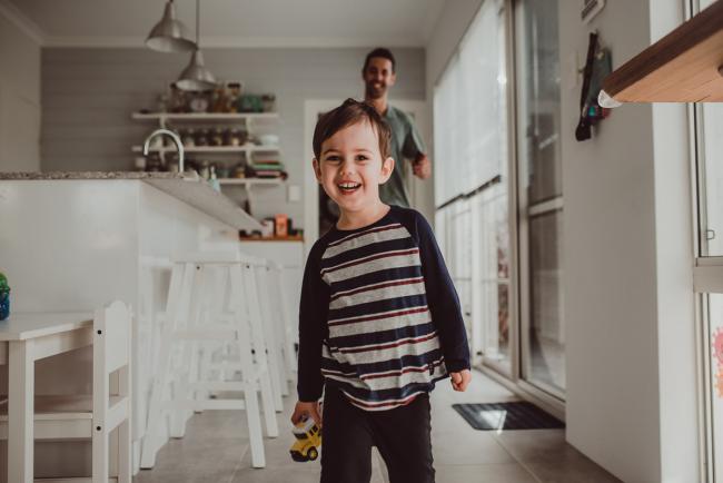 Little boy running and laughing in front of his father with family photographer Perth