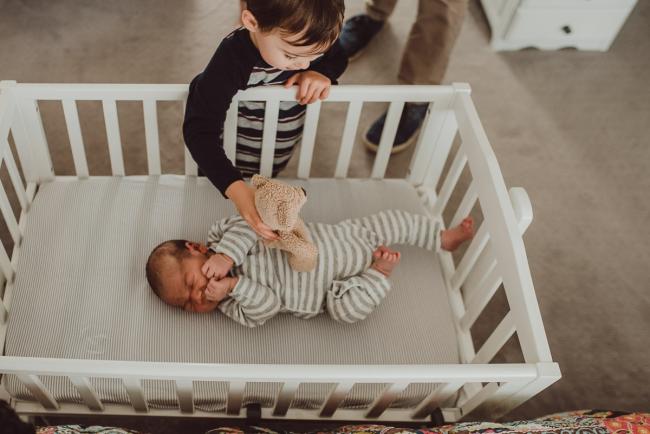 Little boy leaning into the bassinet to his baby brother with Lifestyle Newborn Photographer Perth