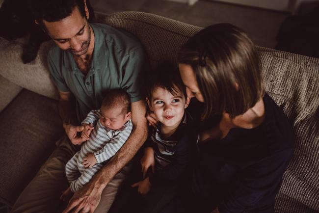 Family of four sitting on a couch with little boy looking at his mother with Lifestyle Newborn Photographer Perth