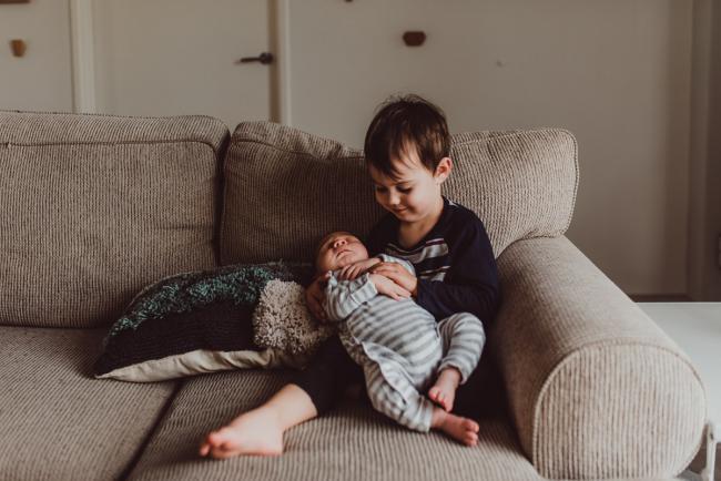 Big brother holding his new baby brother on the couch with Lifestyle Newborn Photographer Perth