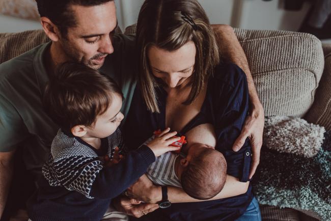 Little boy riding a truck on his mother as she feeds his baby brother with Lifestyle Newborn Photographer Perth