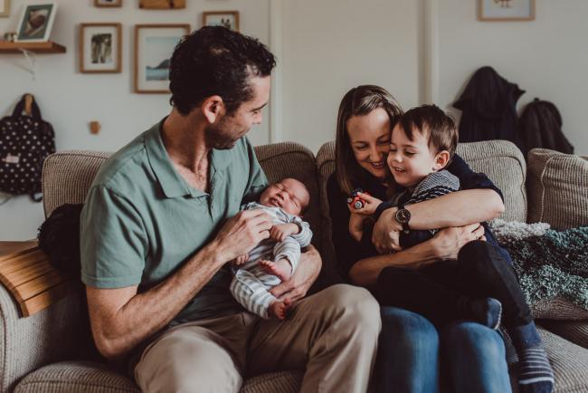 Mother cuddling son as father holds new baby on the couch with Lifestyle Newborn Photographer Perth