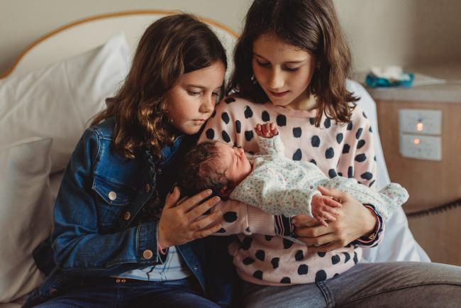 Two sisters holding their new baby sister on the hospital bed with Perth Fresh 48 Photographer at SJOG Mt Lawley