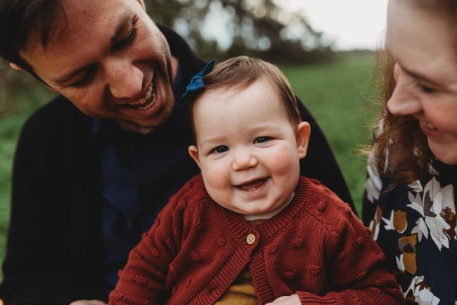 Baby girl smiling as her parents smile at her with Perth family photographer at Perry's Paddock