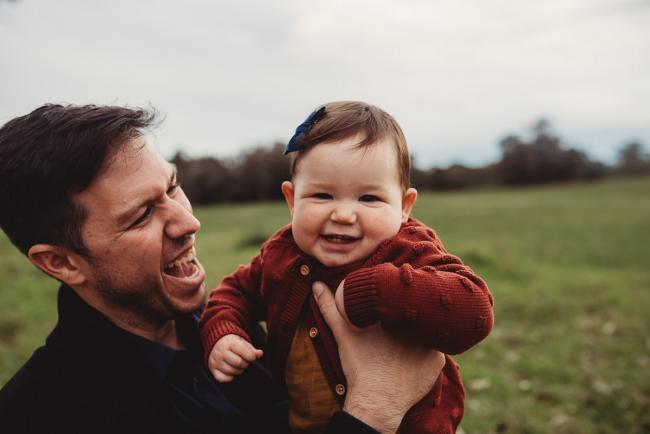 Father laughing at daughter who is smiling at the camera with Perth family photographer at Perry's Paddock