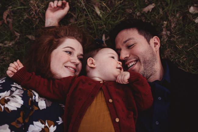 Parents laying on the grass with their daughter between them with Perth family photographer at Perry's Paddock