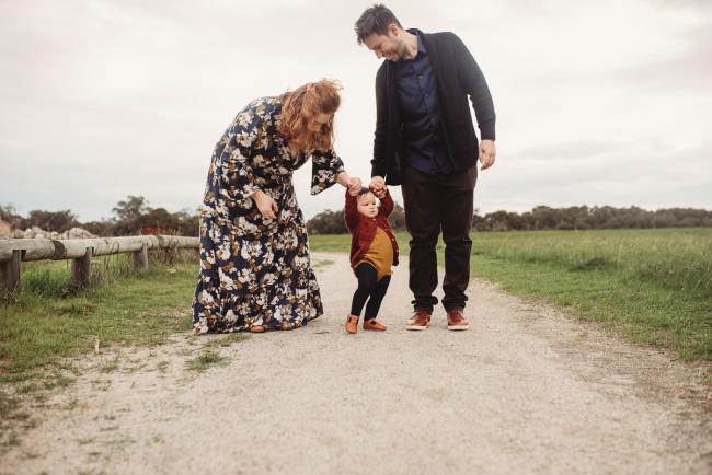 Parents holding the hands of their daughter who is learning to walk with Perth family photographer at Perry's Paddock