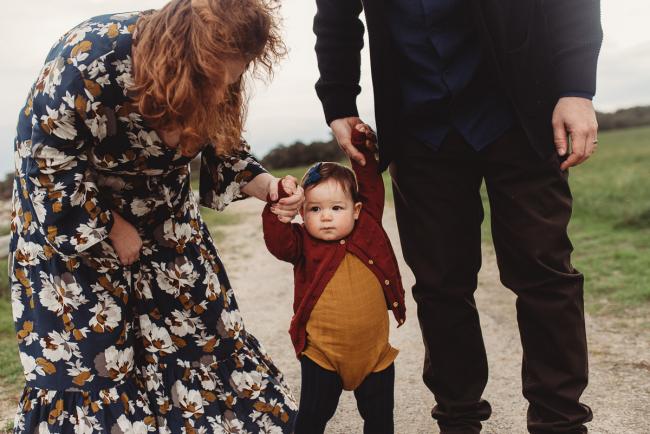 Parents holding the hands of their daughter who is learning to walk with Perth family photographer at Perry's Paddock