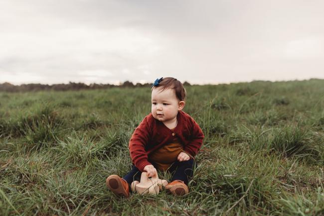 Little girl sitting on grass with Perth family photographer at Perry's Paddock