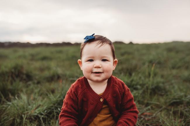 Little girl on grass smiling at camera with Perth family photographer at Perry's Paddock