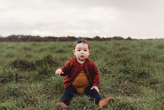 Little girl sitting on grass with Perth family photographer at Perry's Paddock